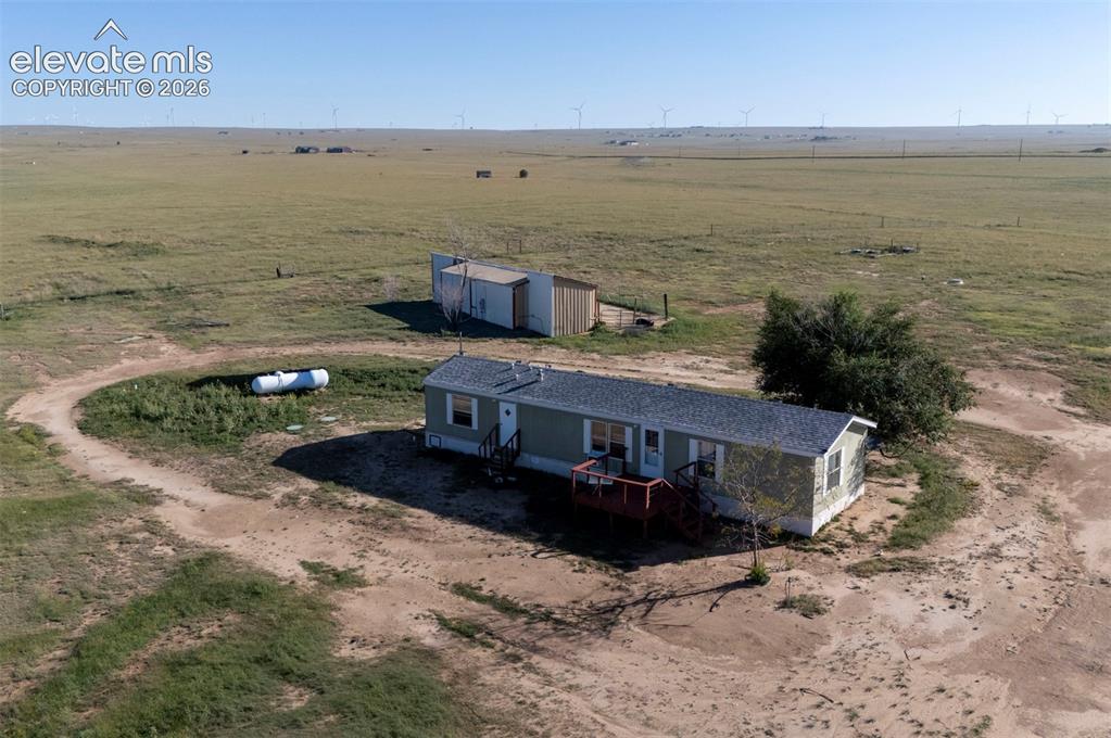 Caption: Expansive rural property featuring a residential structure with a shingled roof, an exterior deck, a