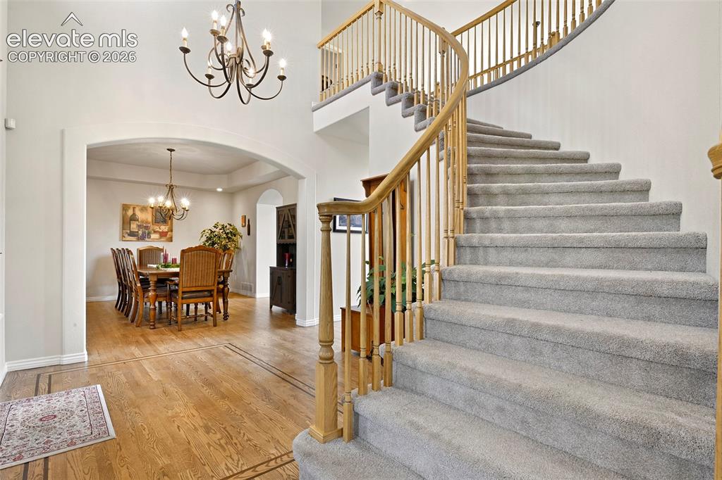 Image 4 of 46: Sweeping staircase in vaulted hardwood foyer, with arched entry to...