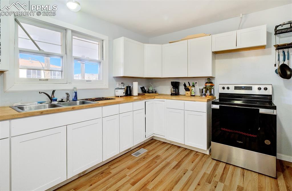 Image 10 of 29: Kitchen featuring white cabinetry, electric range, a sink, light wood-style