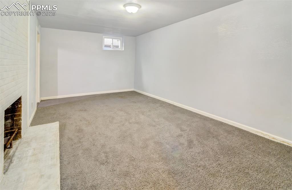 Image 18 of 29: Below grade area with a brick fireplace, carpet, and baseboards