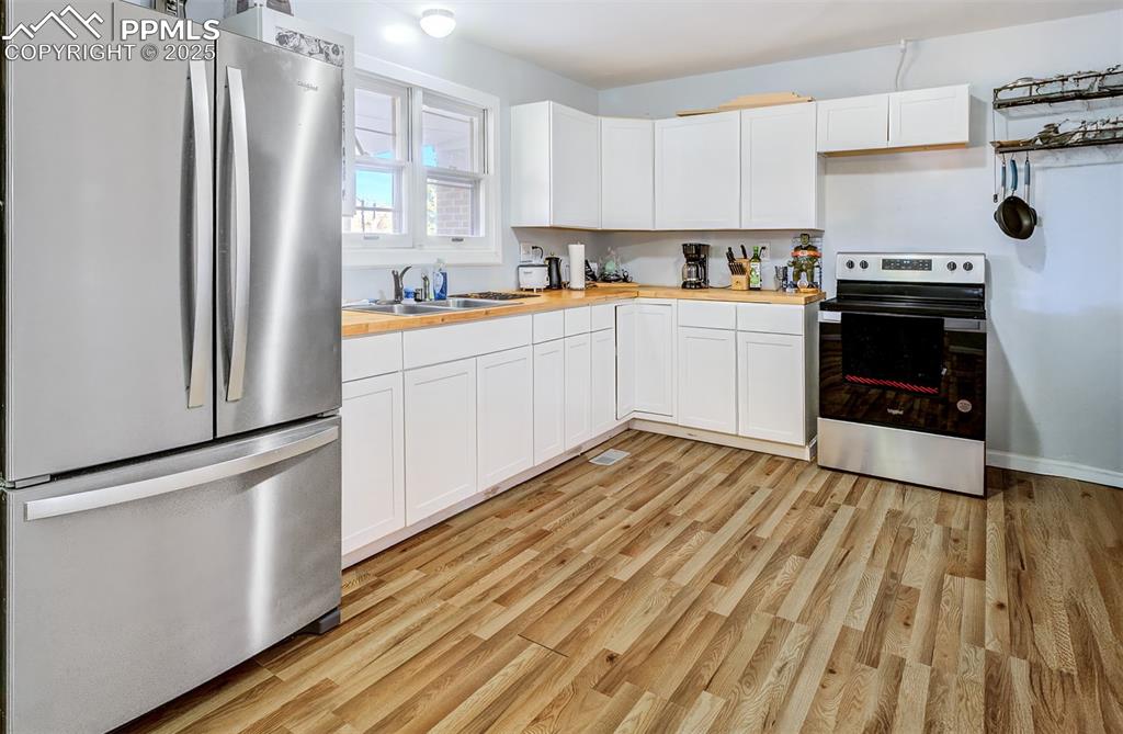 Image 8 of 29: Kitchen with white cabinetry, butcher block countertops, stainless steel ap