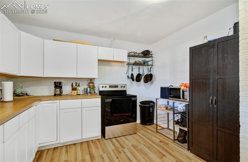 Image 9 of 29: Kitchen with white cabinets, wooden counters, stainless steel range with el