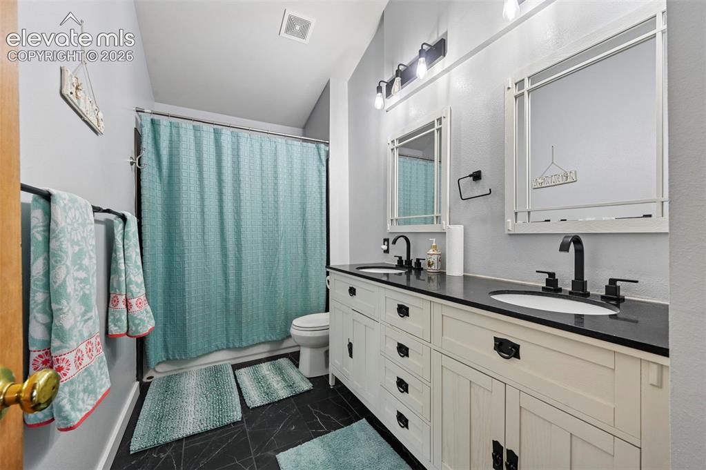 Image 15 of 37: Double vanity featuring integrated sinks, dark countertops, and matte black