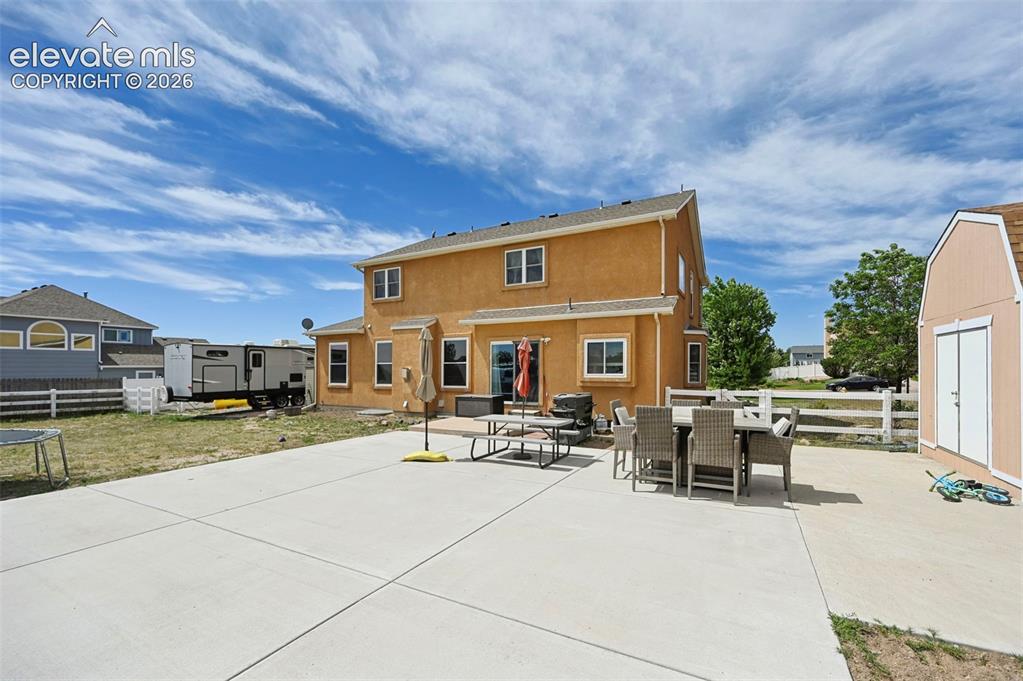 Image 34 of 37: Expansive concrete patio with stucco exterior, rear double doors, multiple