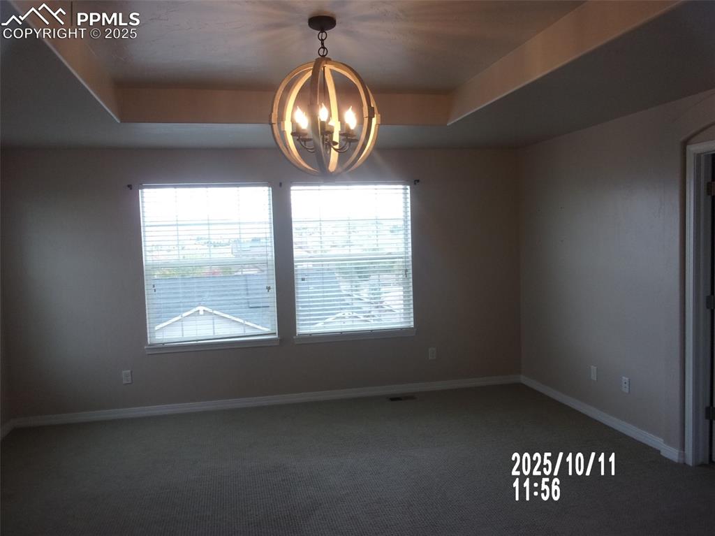 Image 17 of 21: Spare room featuring dark colored carpet, a raised ceiling, and a chandelie