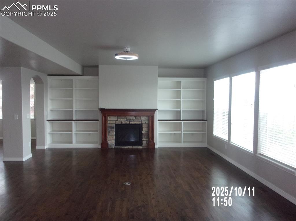 Image 5 of 21: Unfurnished living room featuring arched walkways, a fireplace, and dark wo