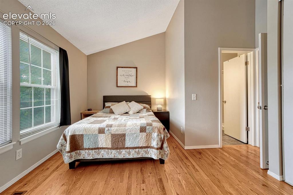 Image 29 of 50: Second bedroom also features hardwood floor, vaulted ceiling, and attached 