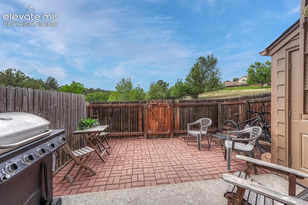 Image 36 of 50: Fully fenced back patio features pavers and garden beds