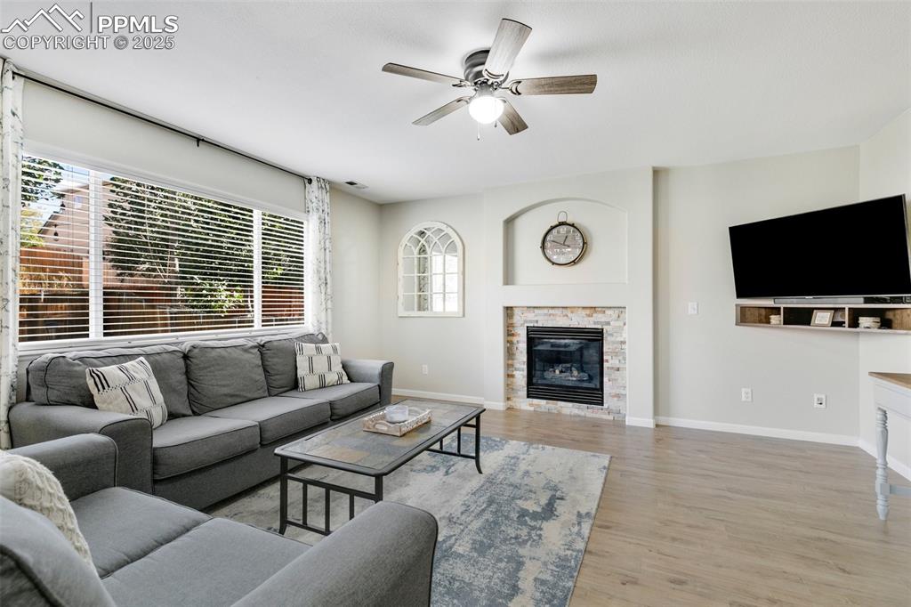 Image 14 of 27: Living area with light wood finished floors, a stone fireplace, and ceiling