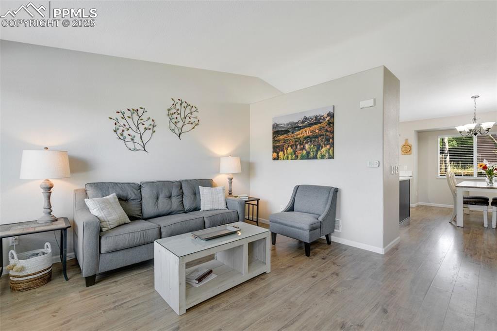 Image 3 of 27: Living room with a chandelier, light wood-style floors, and vaulted ceiling