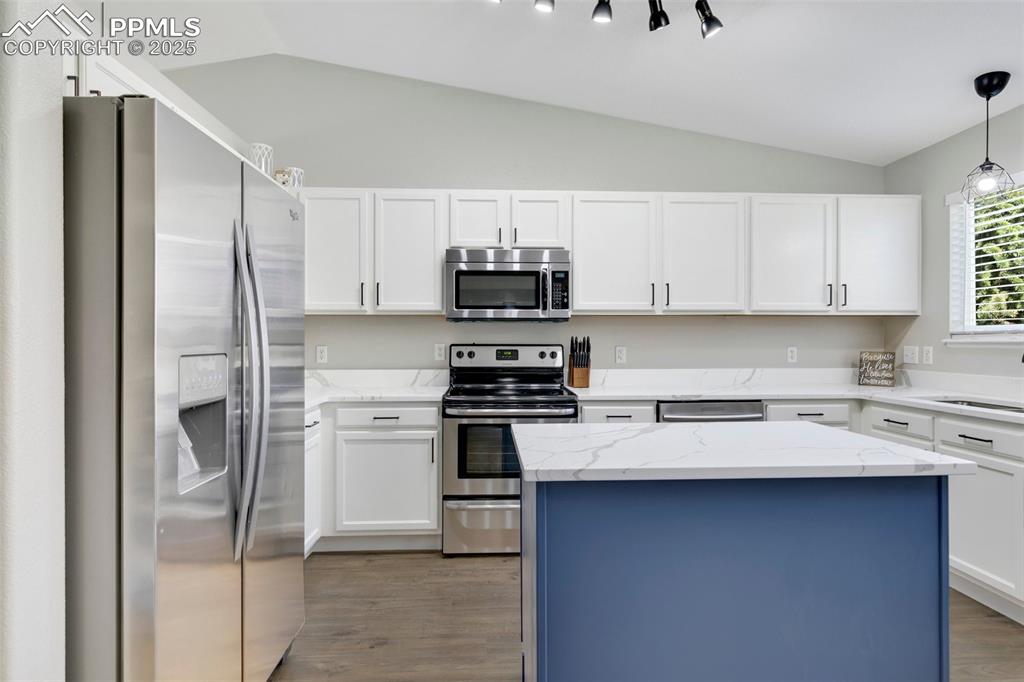 Image 8 of 27: Kitchen with stainless steel appliances, vaulted ceiling, light stone count