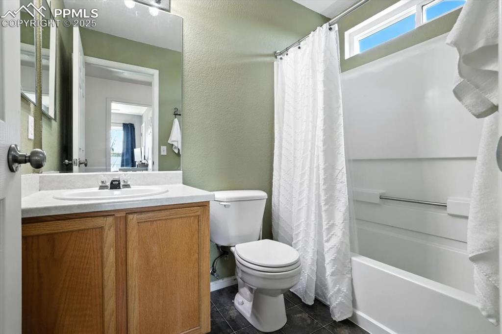 Image 16 of 33: Full bath with shower / tub combo, vanity, a textured wall, and dark tile p