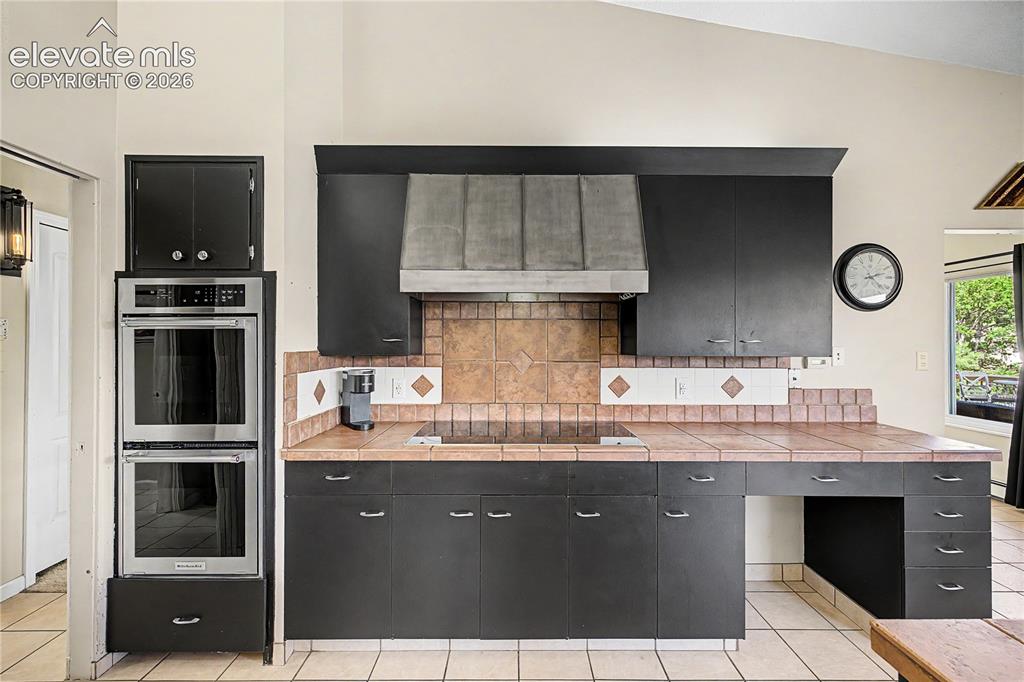 Image 14 of 50: A tile backsplash and a built-in copper range hood pair with modern stainle