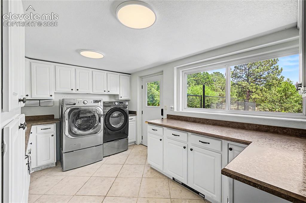 Image 36 of 50: The laundry room is generously sized, with ample cabinetry, a window overlo