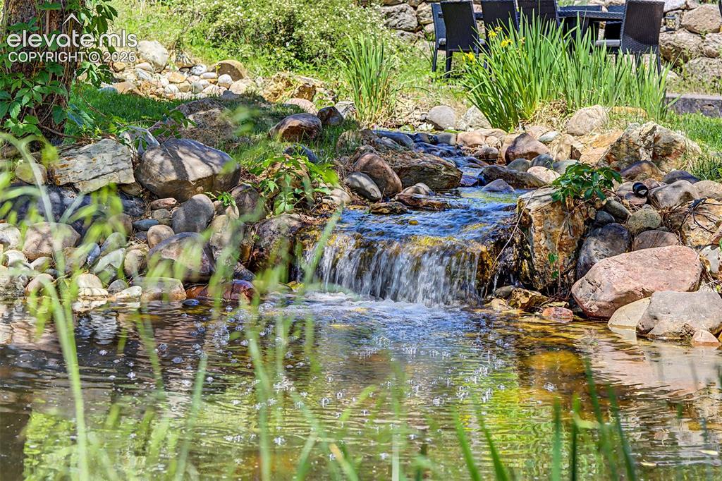 Image 44 of 50: A pond and rock waterfall wind through the yard, bringing the sound of movi