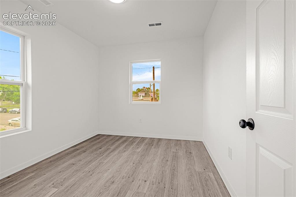 Image 17 of 50: Room featuring wood-finish flooring, two windows, white walls, and a white