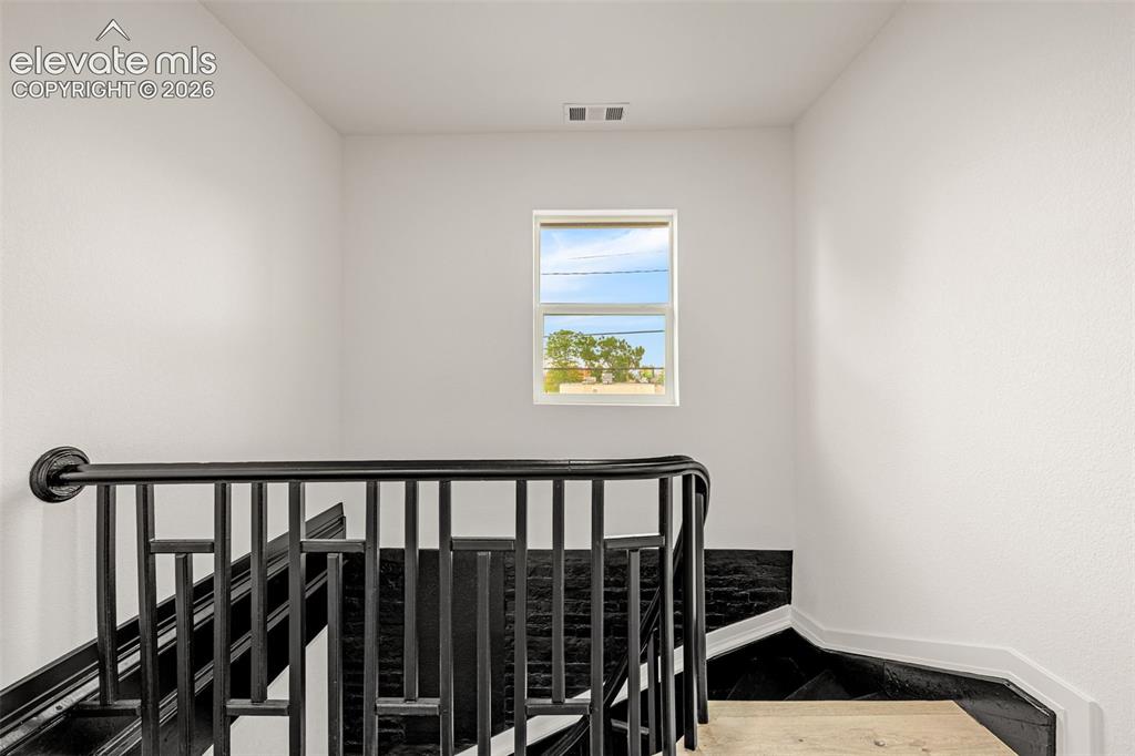 Image 18 of 50: Staircase featuring dark wood-finish treads, a black metal railing, and lig