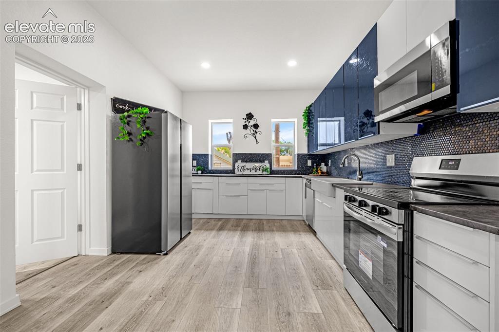 Image 25 of 50: Contemporary kitchen featuring wood-finish flooring, white cabinetry, and d