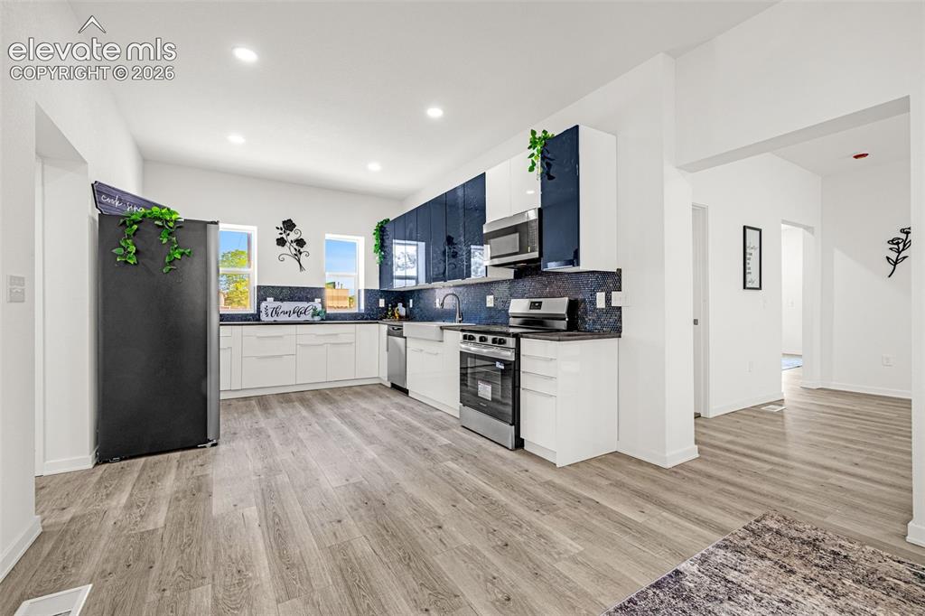 Image 33 of 50: Modern kitchen featuring white cabinetry, dark countertops, and a full suit