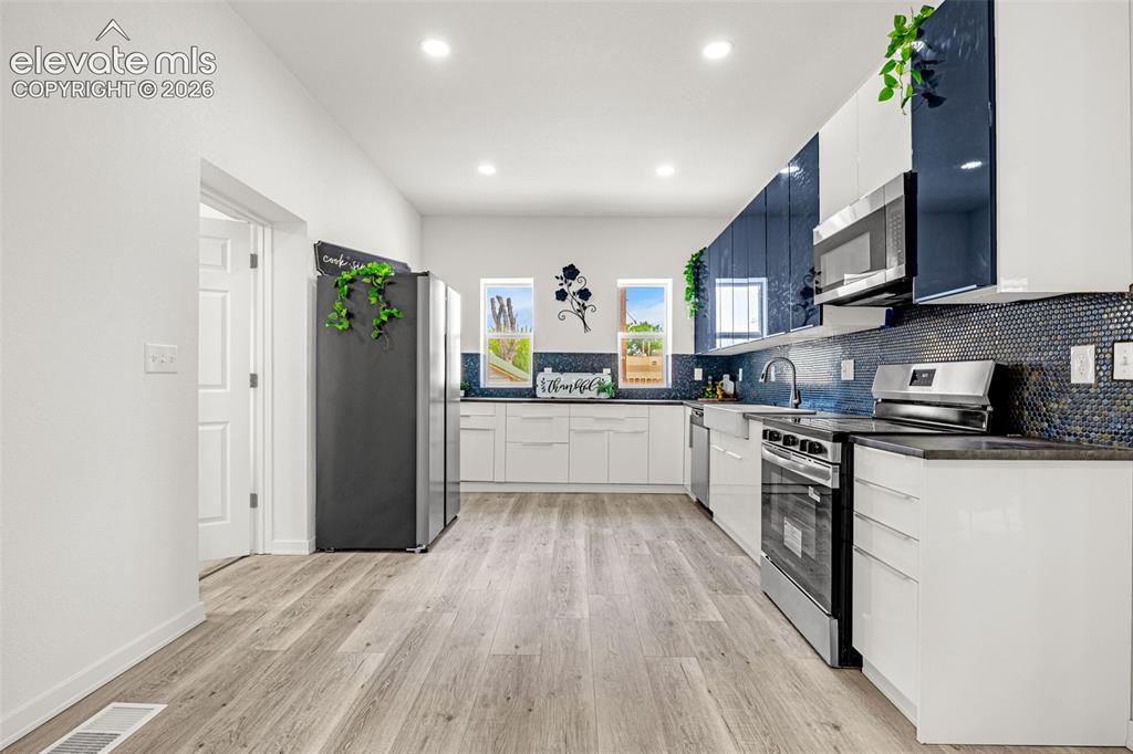 Image 34 of 50: Modern kitchen featuring sleek white cabinetry, a stylish blue mosaic tile