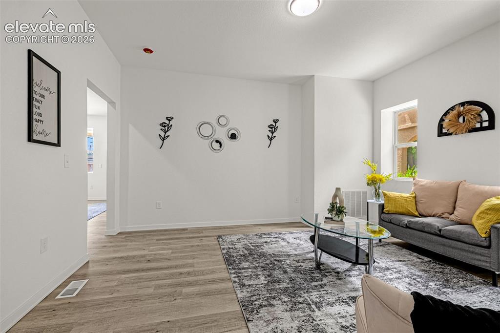 Image 36 of 50: Bright living area featuring wood-finish flooring, white walls, and a visib