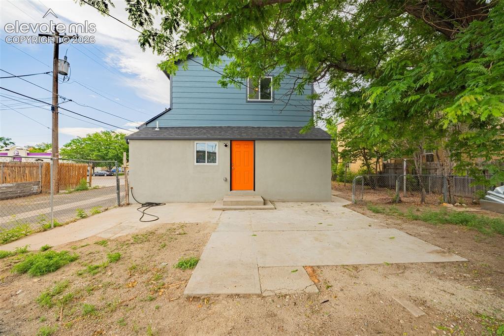 Image 42 of 50: Rear exterior featuring a vibrant orange door, light gray stucco, and blue