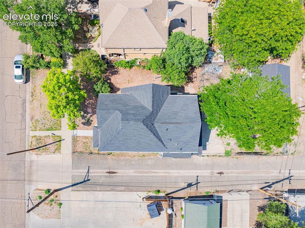 Image 48 of 50: Gabled roofline with dark shingles, set on a lot with mature trees and esta