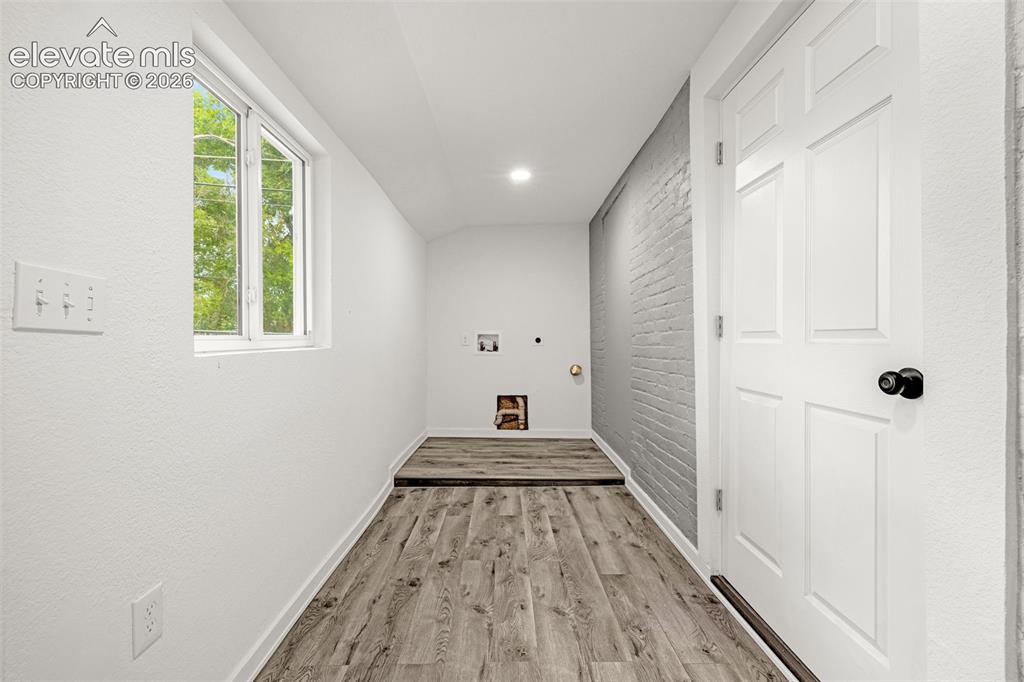 Image 8 of 50: Utility room featuring a painted brick accent wall, wood-finish flooring, a