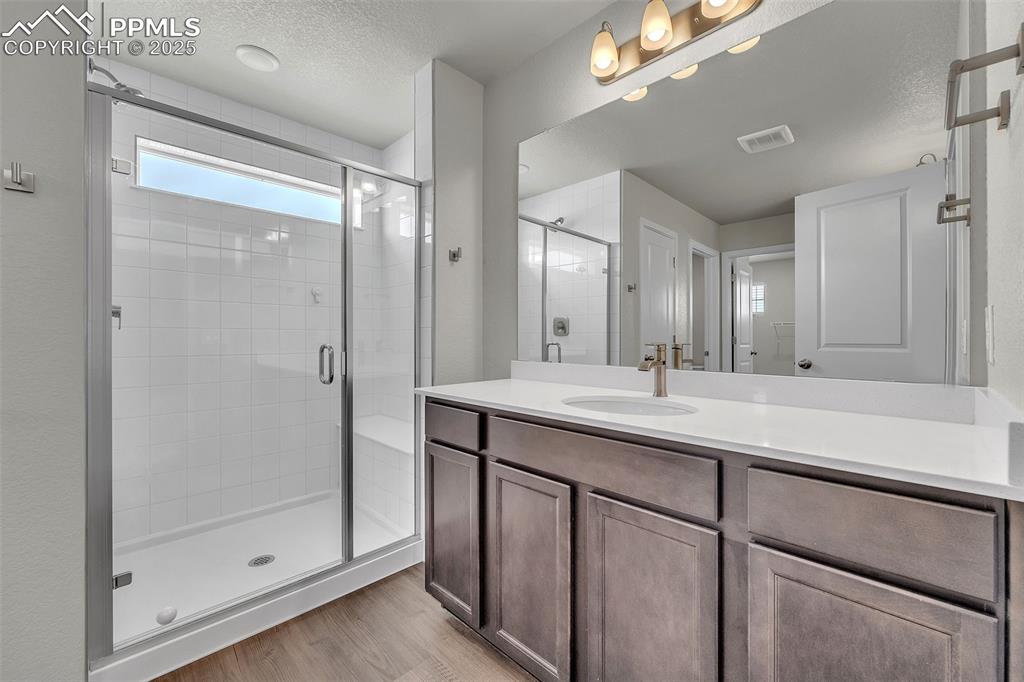 Image 29 of 50: Bathroom featuring a stall shower, vanity, a textured ceiling, and light wo