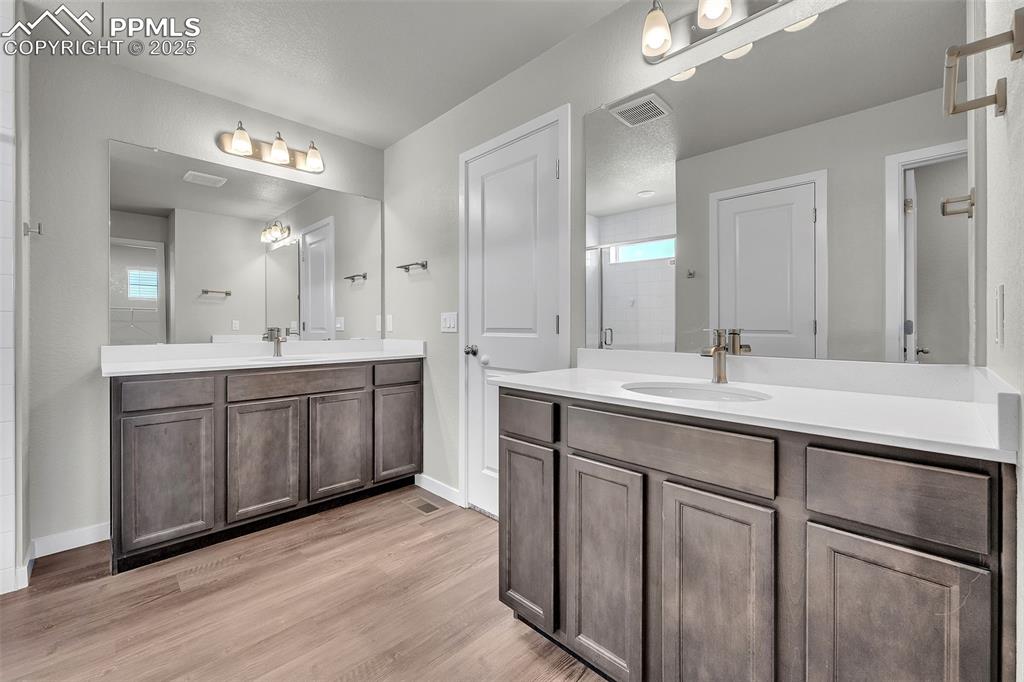 Image 30 of 50: Bathroom with two vanities, a shower stall, light wood-style floors, and a 