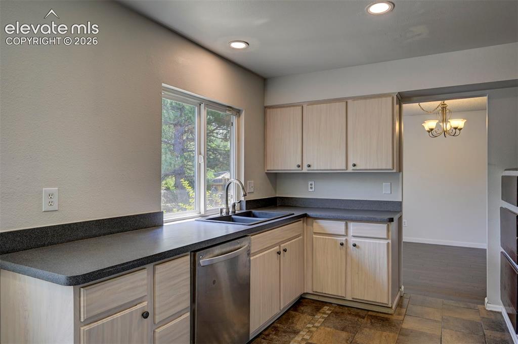 Image 14 of 49: Kitchen featuring light wood-finish cabinetry, dark countertops, and a stai