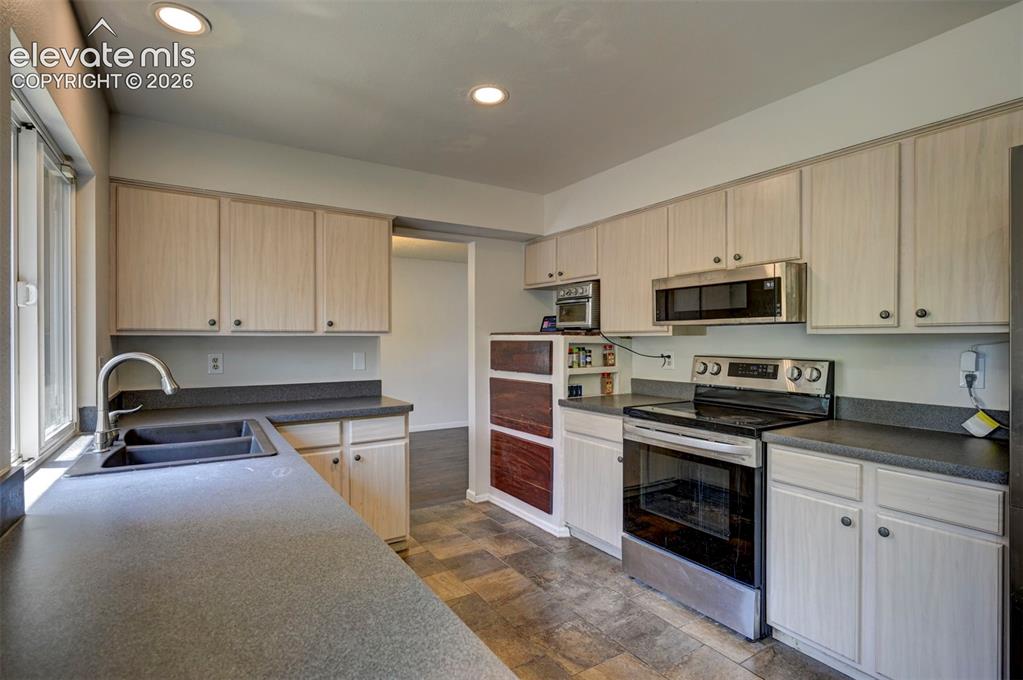 Image 15 of 49: Kitchen featuring white cabinetry, dark countertops, a double basin sink wi