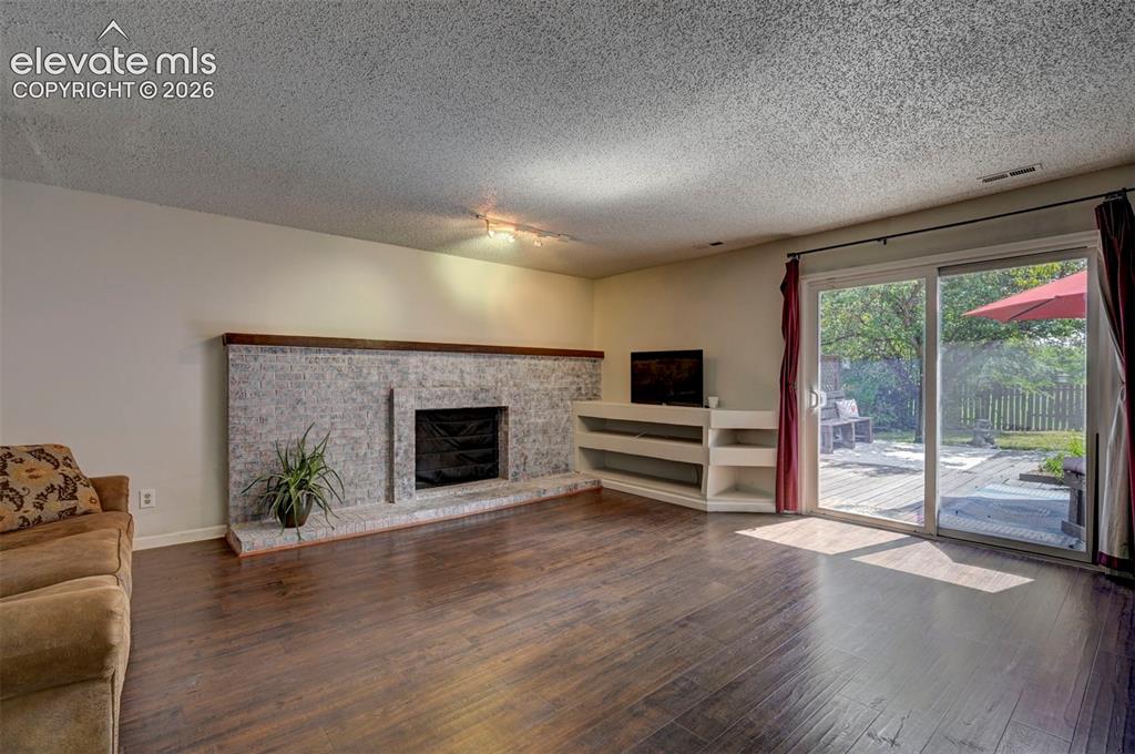 Image 20 of 49: Wood-finish flooring, stone-clad fireplace, integrated shelving, and slidin