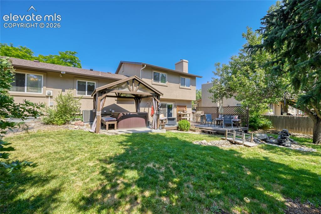 Image 42 of 49: Expansive backyard featuring a manicured lawn, a built-in wooden deck, and 