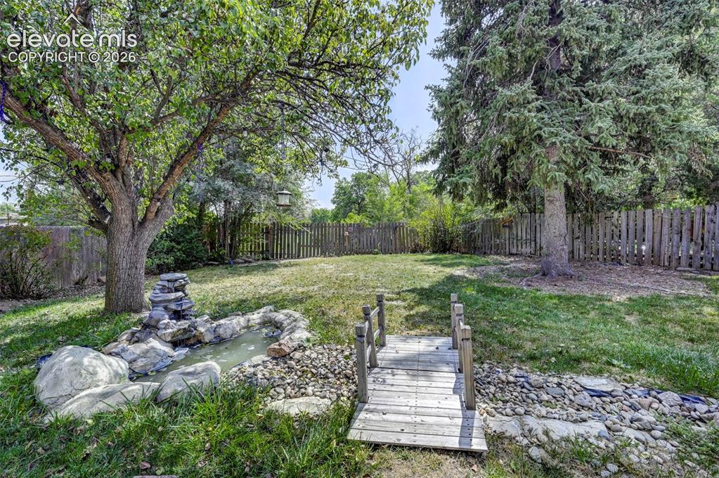 Image 43 of 49: Expansive backyard featuring a rock water feature, decorative wooden bridge