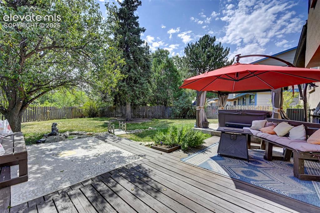 Image 45 of 49: Expansive backyard featuring a wood deck, concrete patio, mature trees, and