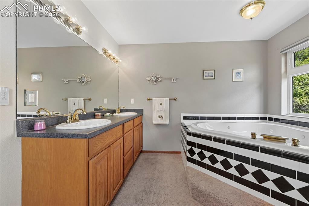 Image 12 of 25: Bathroom featuring a built-in jetted tub with tile surround, dual vanity wi