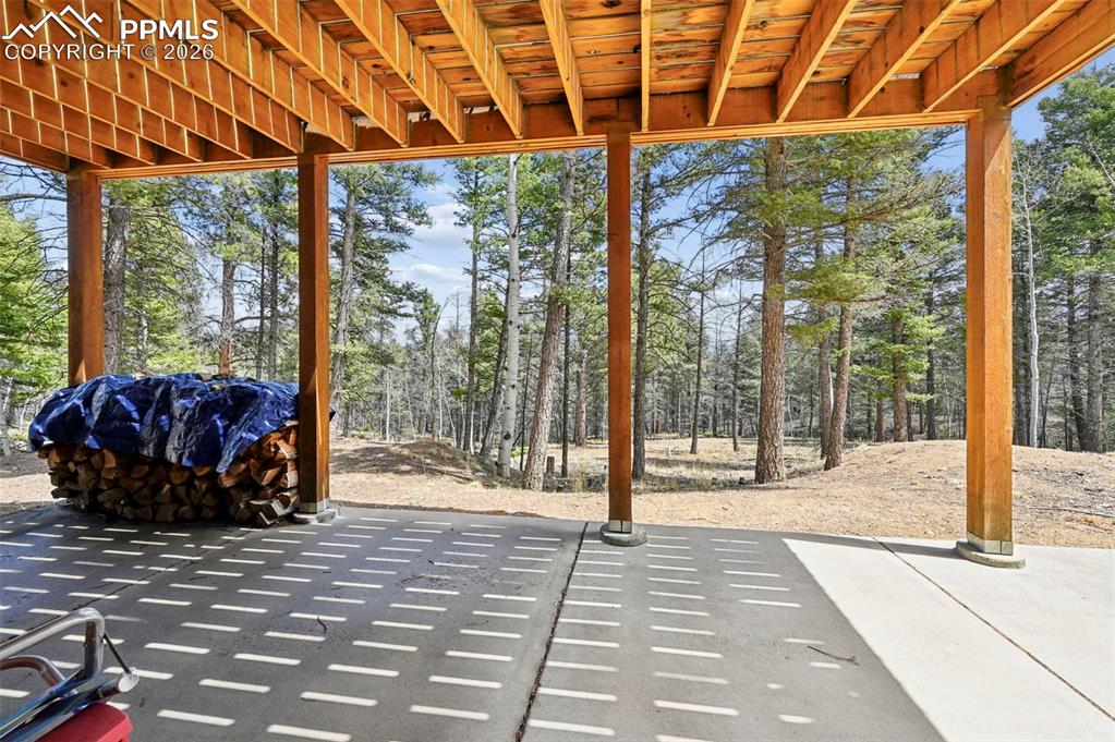 Image 18 of 25: Covered patio featuring a concrete surface, exposed wood beam ceiling, and 