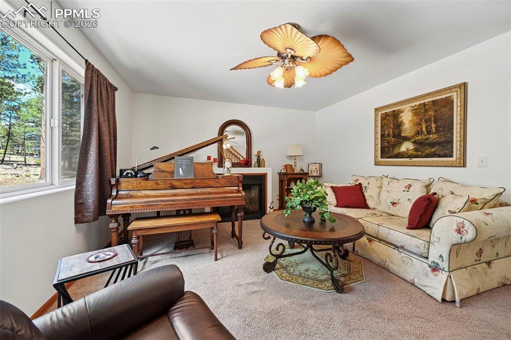 Image 7 of 25: Carpeted living area featuring a fireplace with a wood mantel, a window off