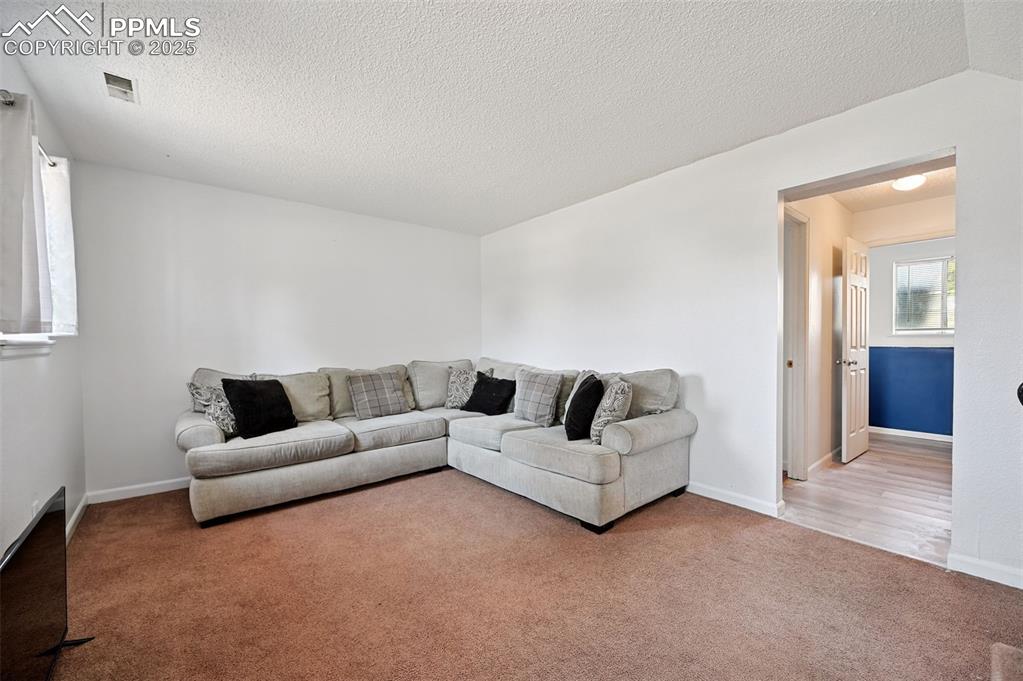 Image 7 of 19: Carpeted living room featuring a textured ceiling and baseboards
