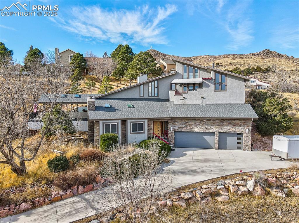 Caption: View of front facade featuring stone siding, concrete driveway, roof with shingles, a garage, and a 