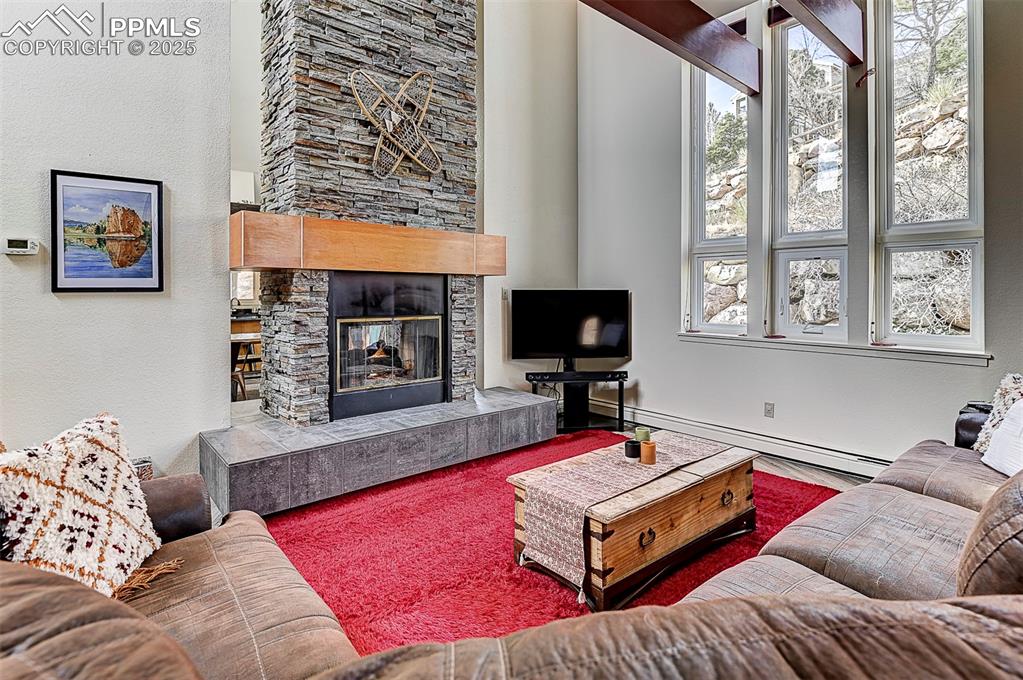 Image 12 of 42: Living room on main-level featuring a two-way tiled fireplace and a baseboa