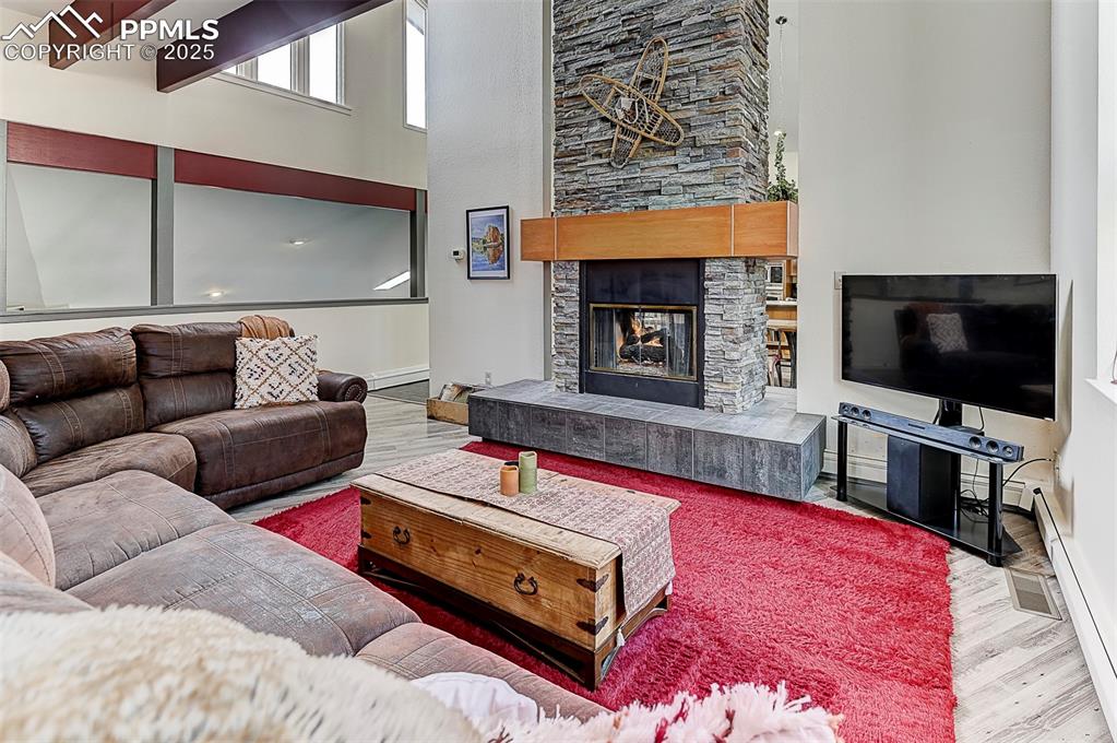 Image 13 of 42: Living area with wood finished floors, a stone fireplace, a high ceiling, a