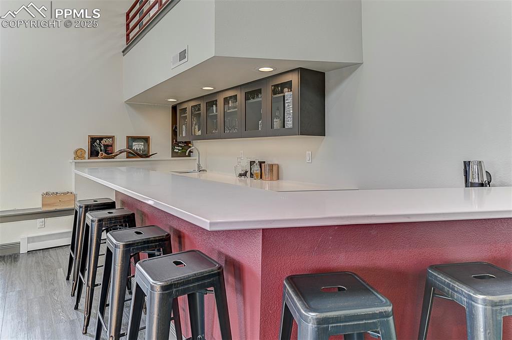Image 8 of 42: Bar area featuring marble, glass insert cabinets, and light wood-style floo