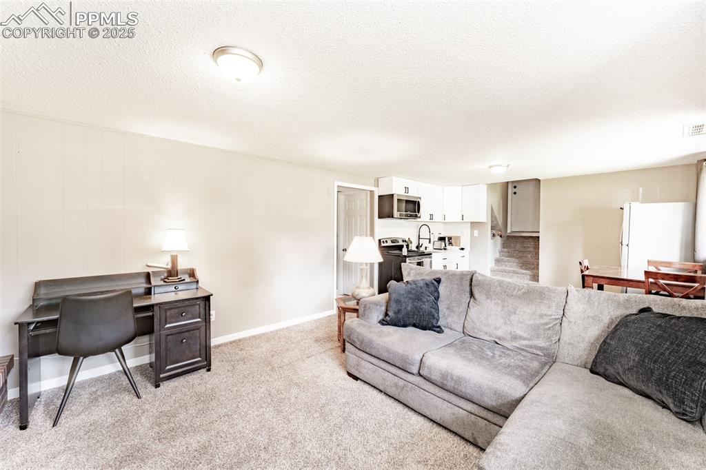 Image 25 of 39: Living room featuring a textured ceiling, light colored carpet, and an offi
