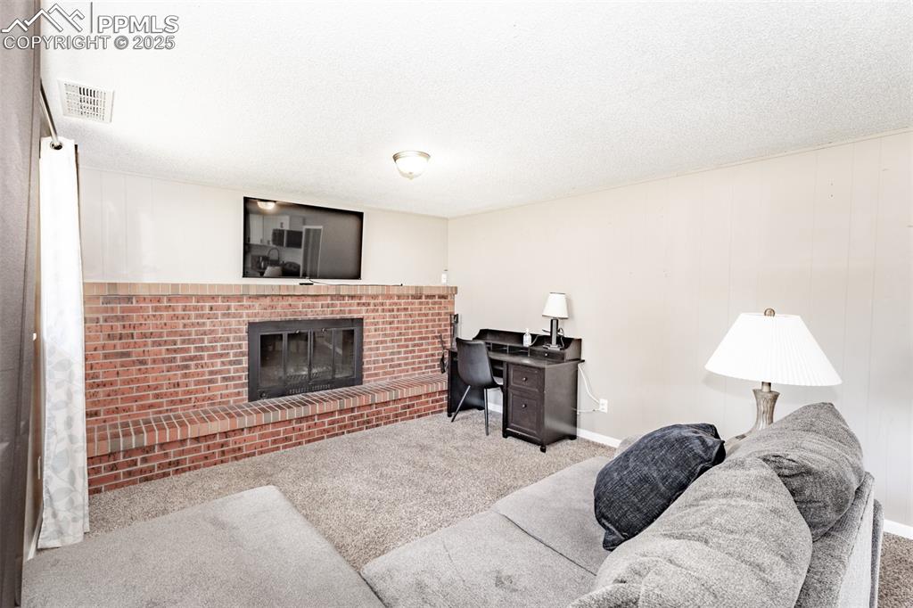 Image 30 of 39: Carpeted living room with a brick fireplace, a textured ceiling, and an off