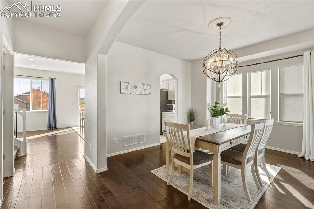 Image 10 of 41: Dining space featuring arched walkways, dark wood-style floors, and a chand
