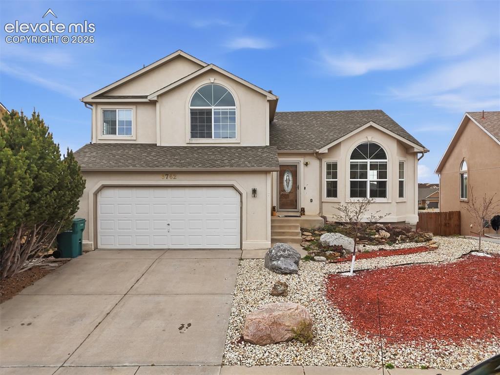 Caption: Stucco exterior with an attached two-car garage, concrete driveway, and a xeriscaped front yard feat