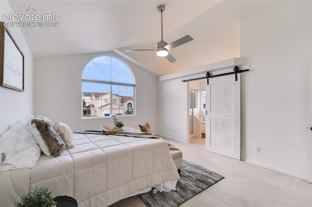 Image 17 of 47: Vaulted ceiling, arched window, ceiling fan, carpet flooring, and barn door