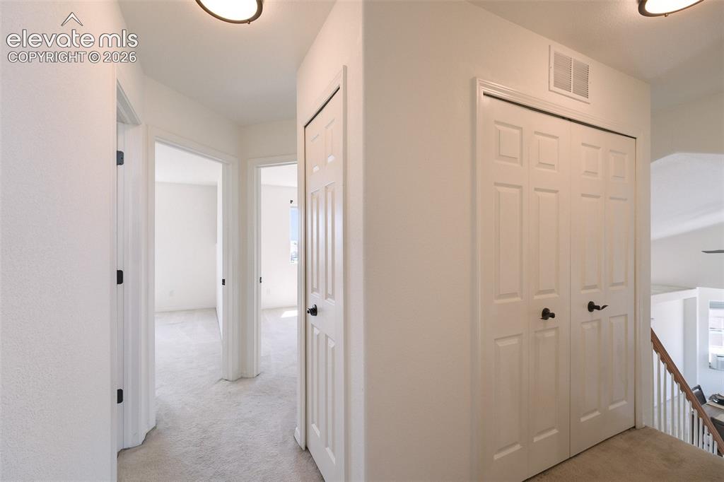 Image 24 of 47: Hallway featuring light-colored carpet flooring, white paneled doors with b